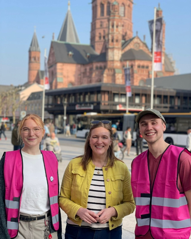 auf dem Bild sind von links nach rechts zu sehen: Leah Krieger – Männer*beratung Mainz, Katharina Binz – Ministerin für Familie, Frauen, Kultur und Integration sowie Stellvertretende Ministerpräsidentin des Landes Rheinland-Pfalz, Jassin Queiroz de Souza – Männer*beratung Mainz, auf dem Mainzer Gutenbergplatz